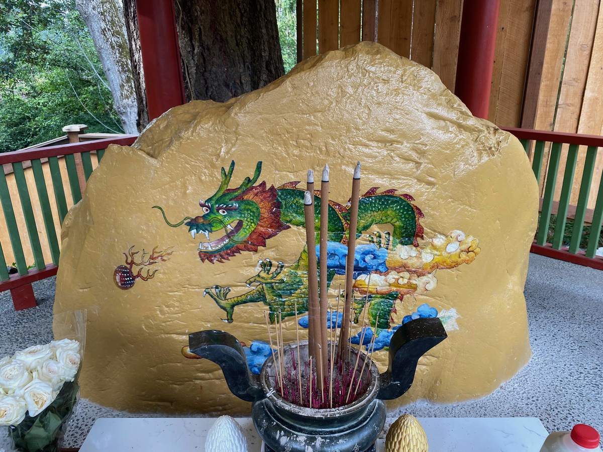 La Pierre de la Divinité Dragon : un grand rocher peint en or, orné d'un dragon vert tendu vers une perle flamboyante, des bâtons d'encens brûlant dans un encensoir devant lui