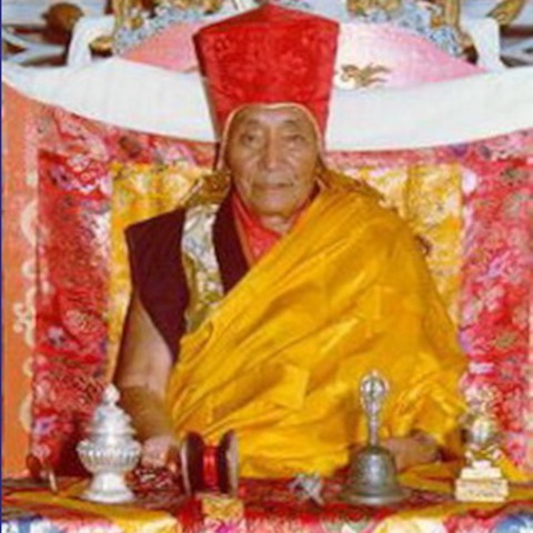 Le maître Sakya Zhengkong, Son Éminence Dezhung Rinpoche, assis devant un autel, coiffé du chapeau rouge de pandita