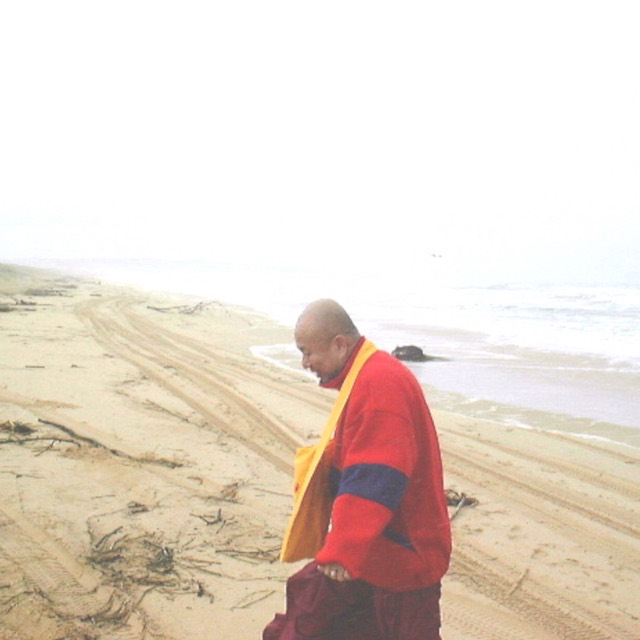 A solitary figure in red robes walking a grey shoreline